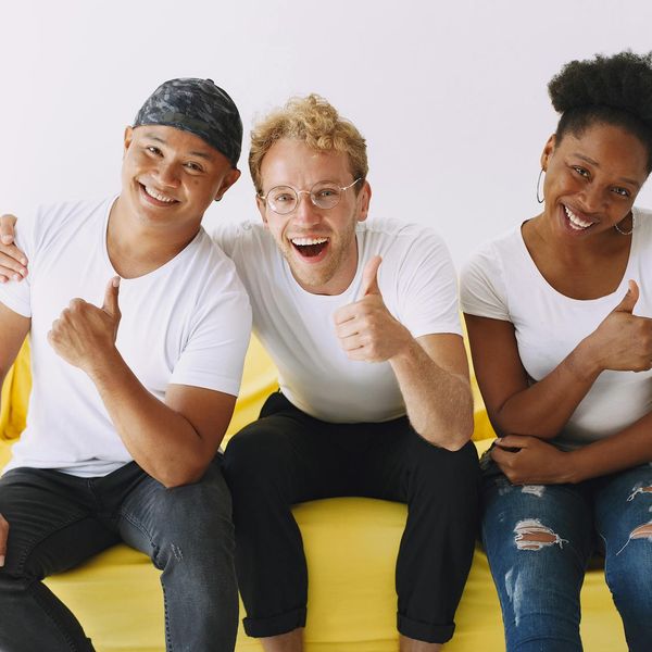 A diverse group of people smiling and sitting on yoga mats in a bright studio.